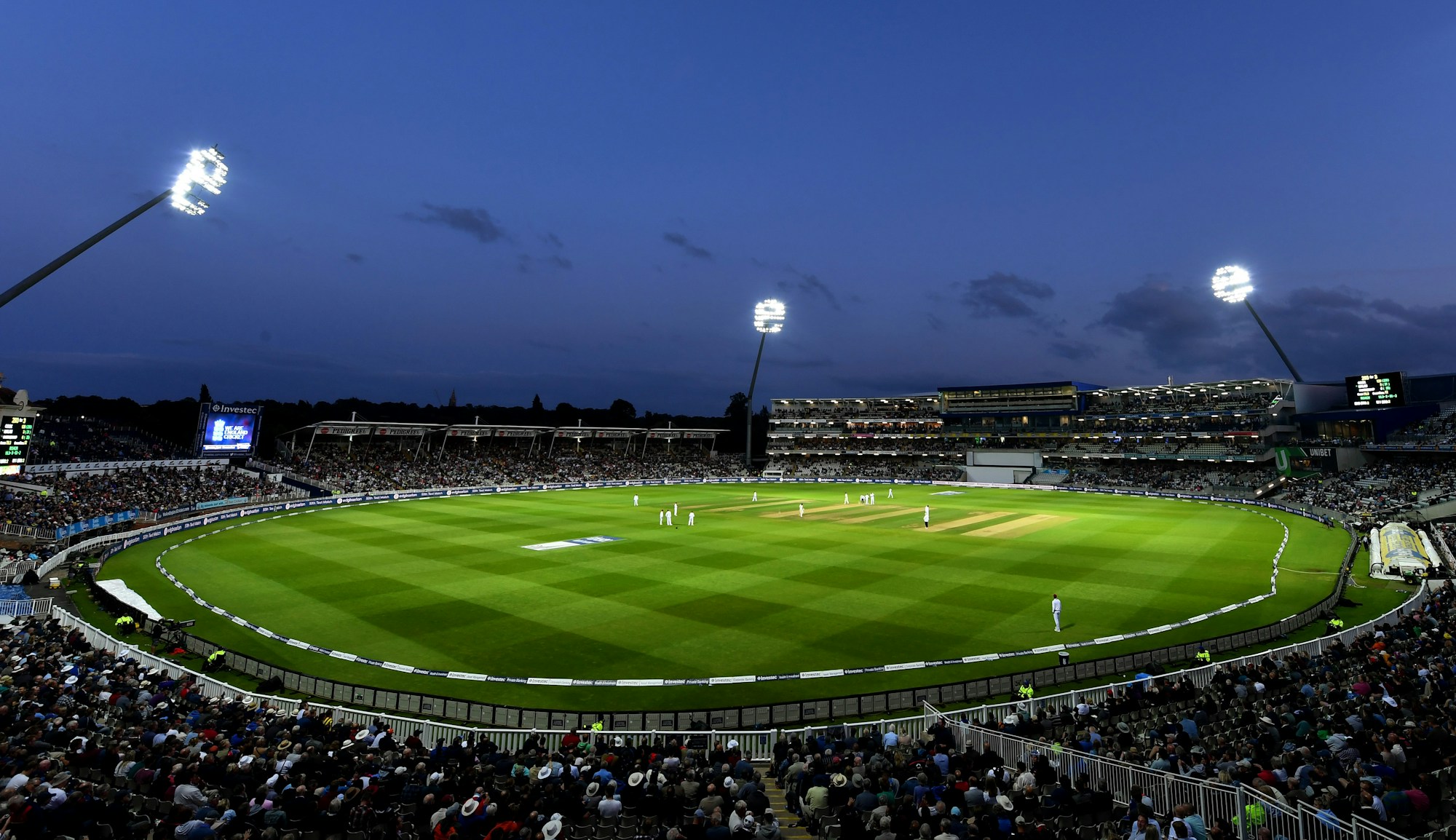 Cricket match on a green pitch in a stadium under floodlights